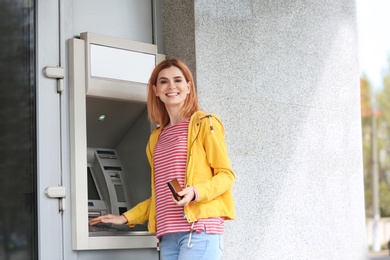 Beautiful woman using cash machine for money withdrawal outdoors. Space for text