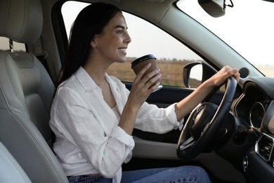 Beautiful young woman with cup of coffee driving her modern car