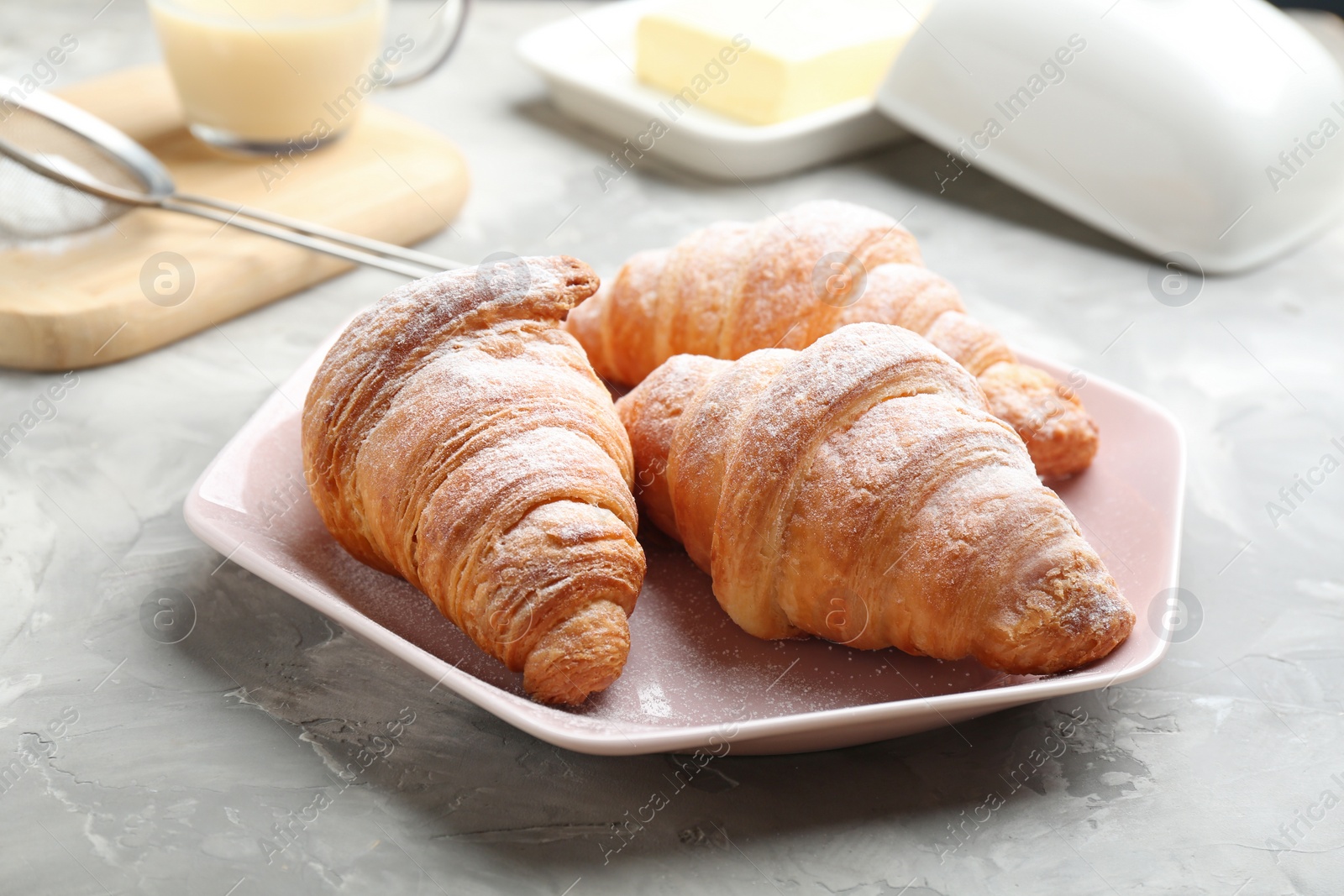 Photo of Plate of fresh croissants sprinkled with powdered sugar on grey table. French pastry