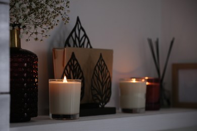 Burning candles. flowers and decor on white shelf