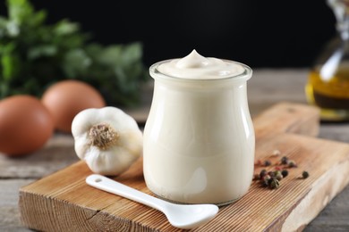 Fresh mayonnaise sauce in glass jar and ingredients on wooden table, closeup