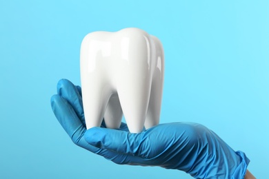 Dentist holding ceramic model of tooth on color background