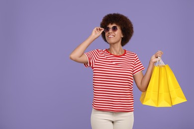 Photo of Happy young woman in stylish sunglasses with shopping bags on purple background. Space for text