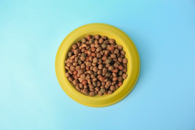 Dry pet food in feeding bowl on light blue background, top view