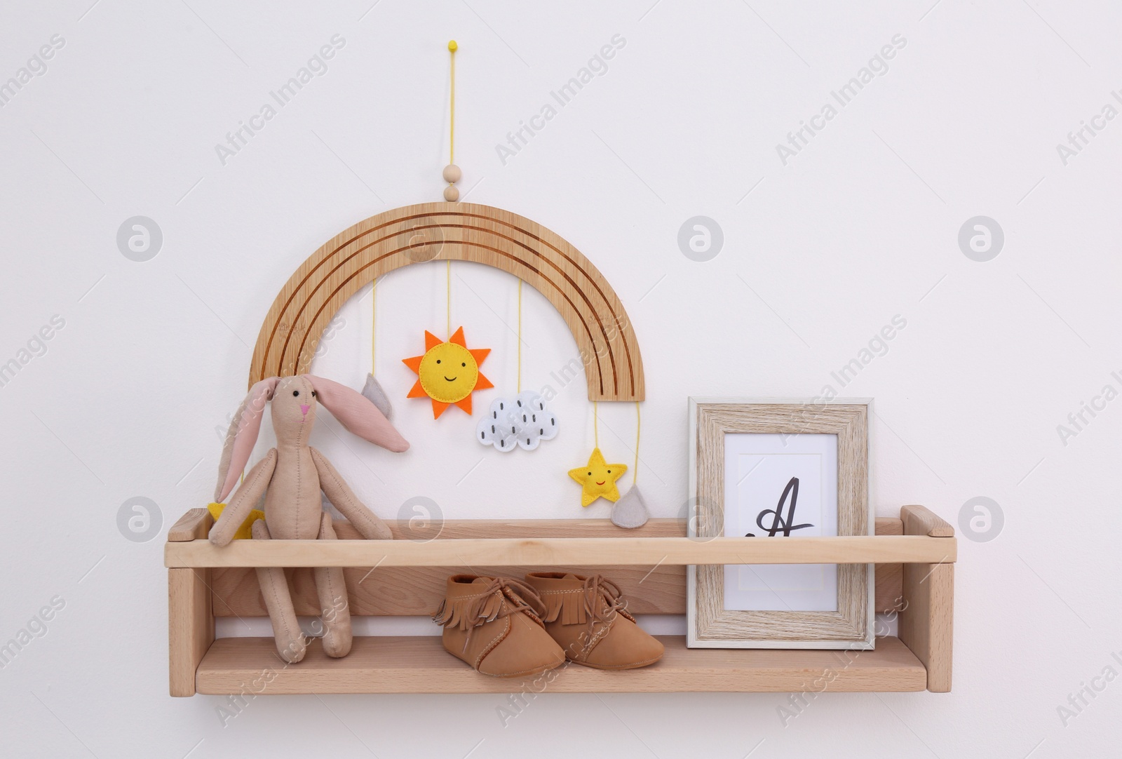 Photo of Wooden shelf with child's booties, toys and photo frame on white wall. Interior element