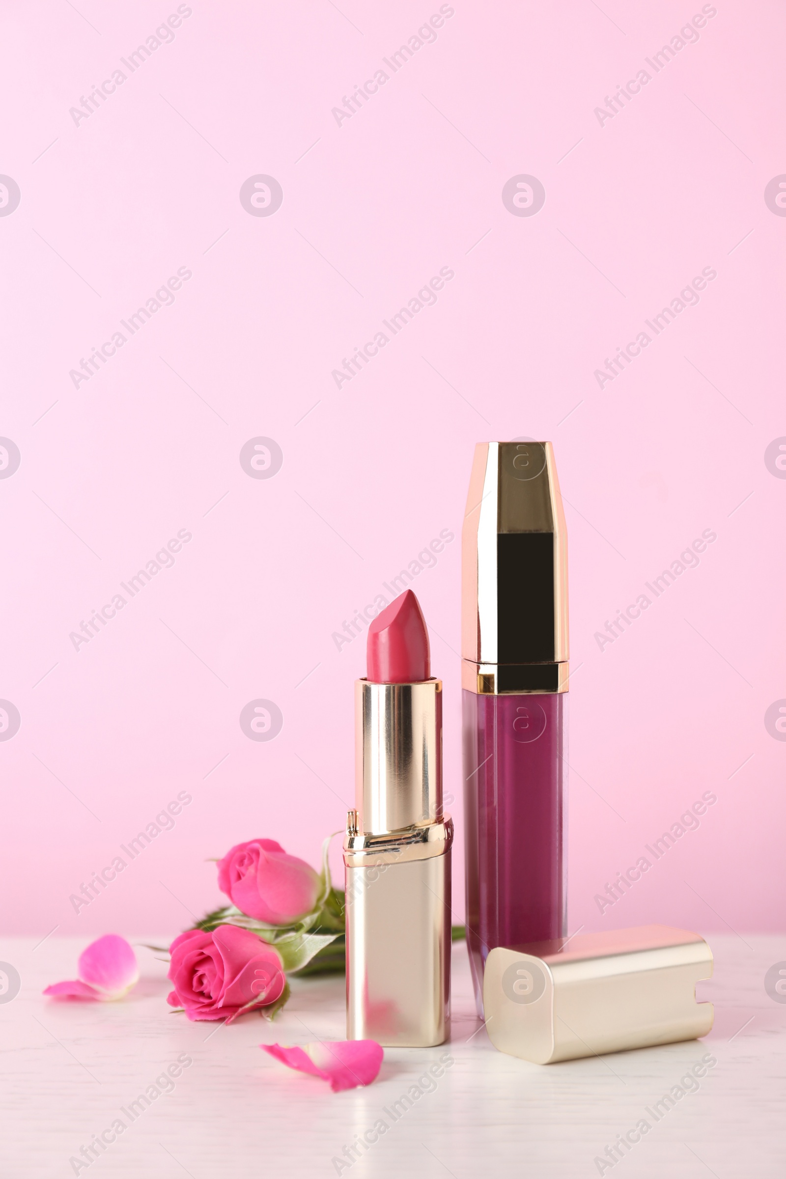 Photo of Lipstick and lip gloss with flowers on table