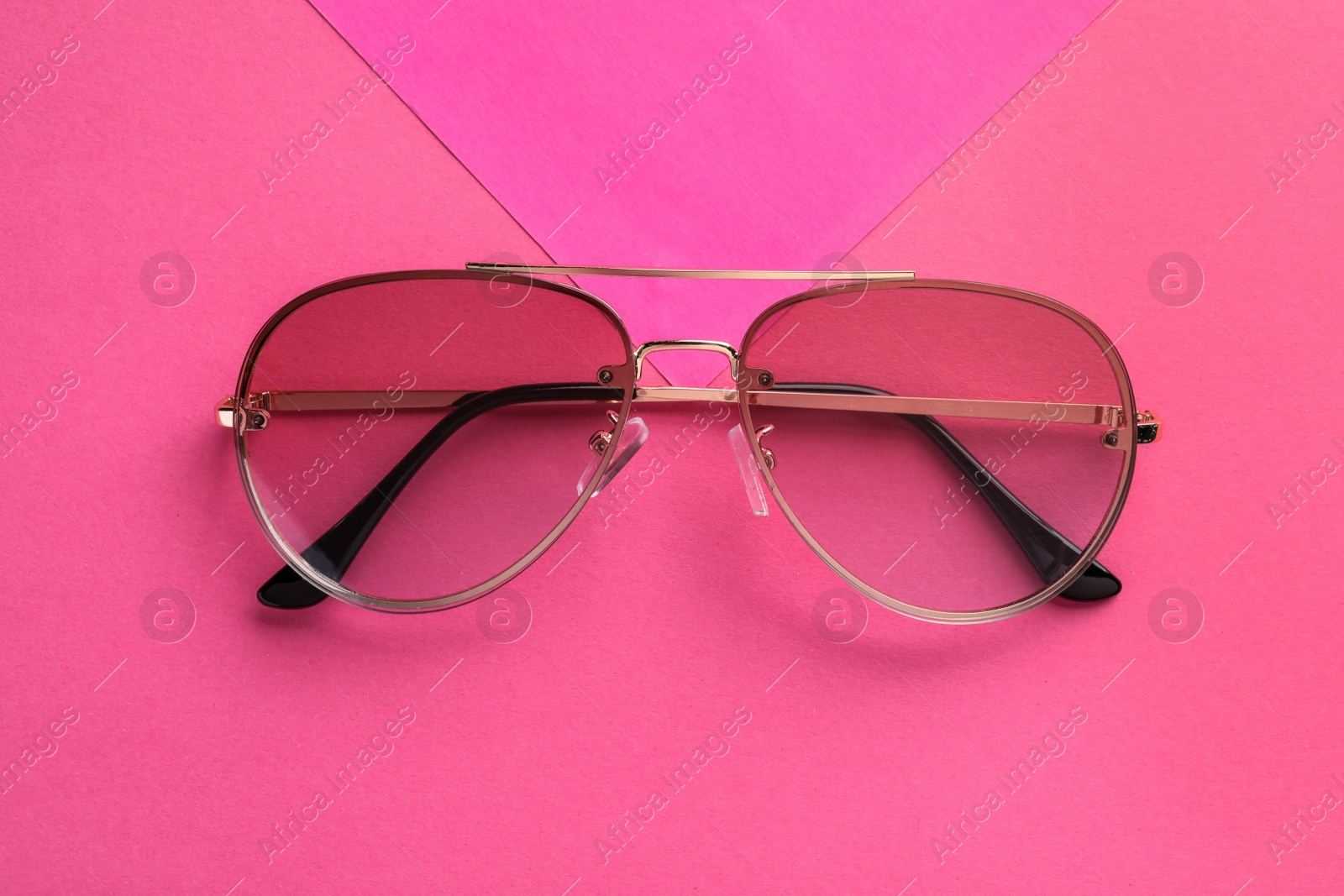 Photo of New stylish sunglasses on pink background, top view