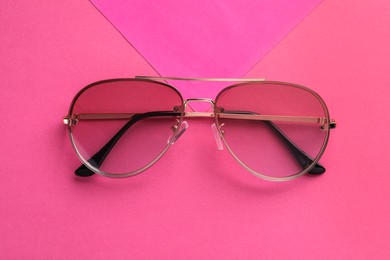 Photo of New stylish sunglasses on pink background, top view