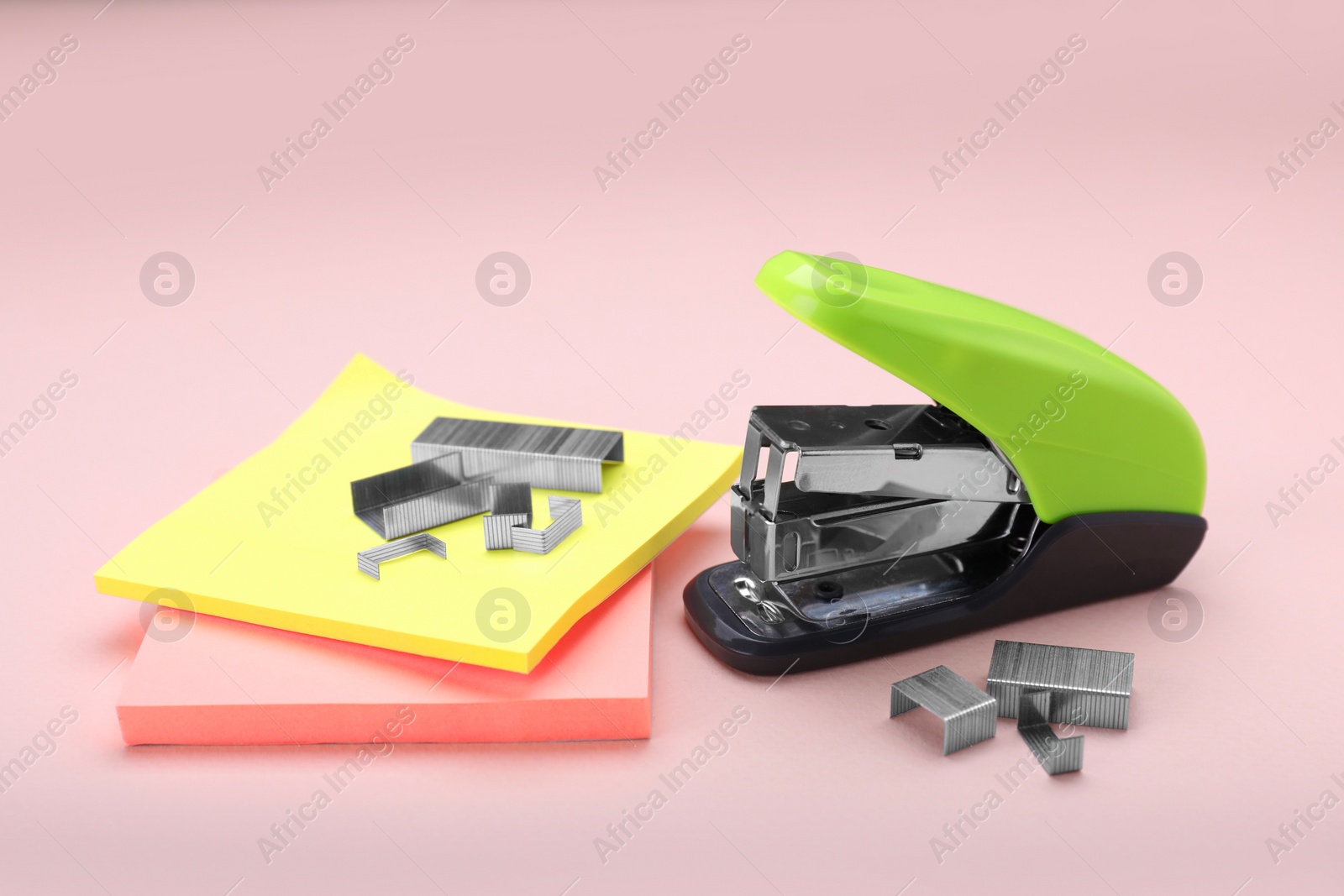 Photo of New bright stapler with staples and sticky notes on pink background. School stationery