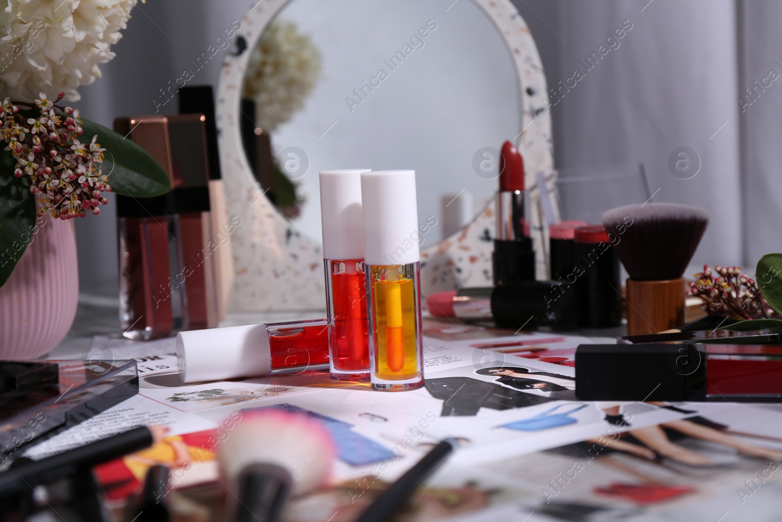 Photo of Bright lip glosses among different cosmetic products and fashion magazine on table indoors