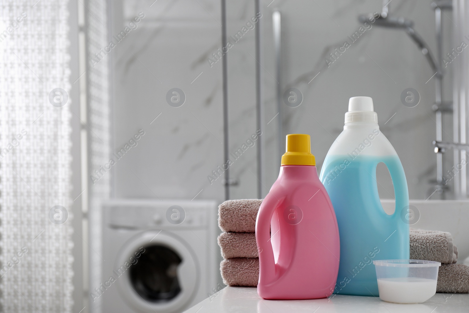 Photo of Stack of folded towels and detergents on white table in bathroom, space for text