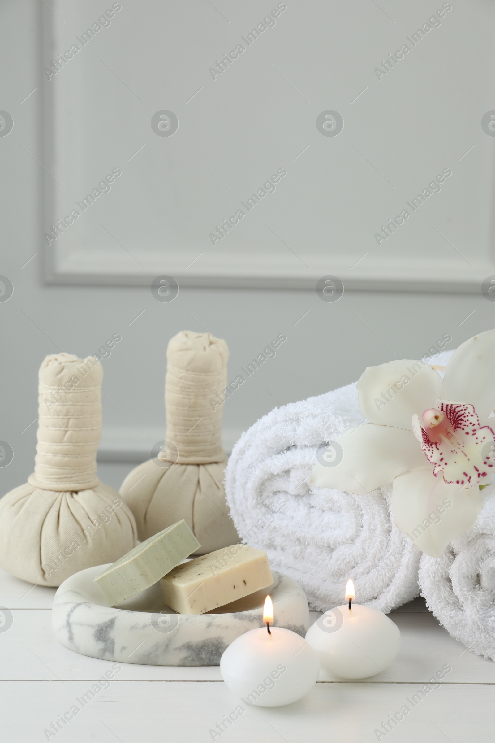 Photo of Beautiful spa composition. Towels, herbal bags, soap bars and burning candles on white wooden table