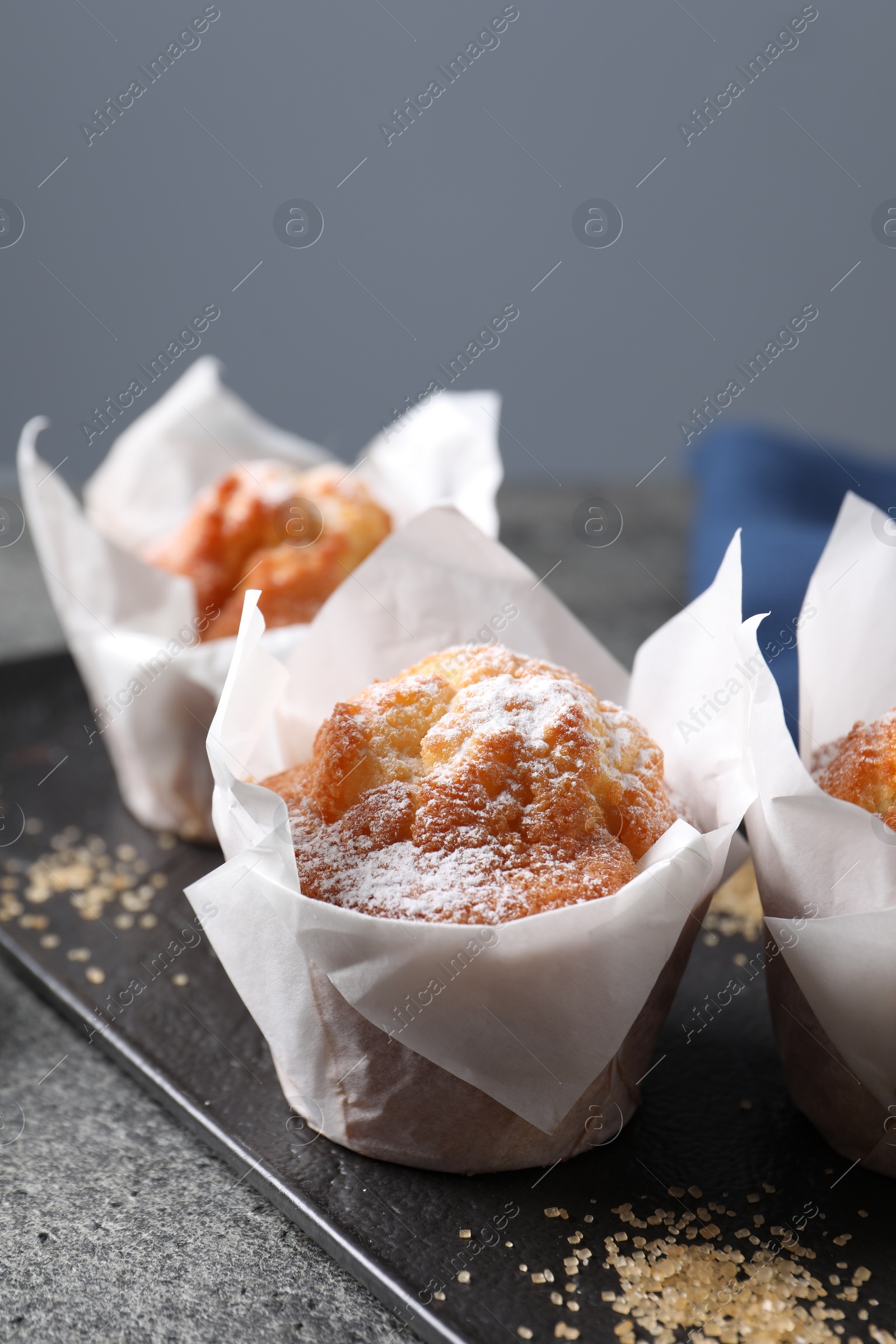 Photo of Delicious muffins with powdered sugar on grey table, closeup