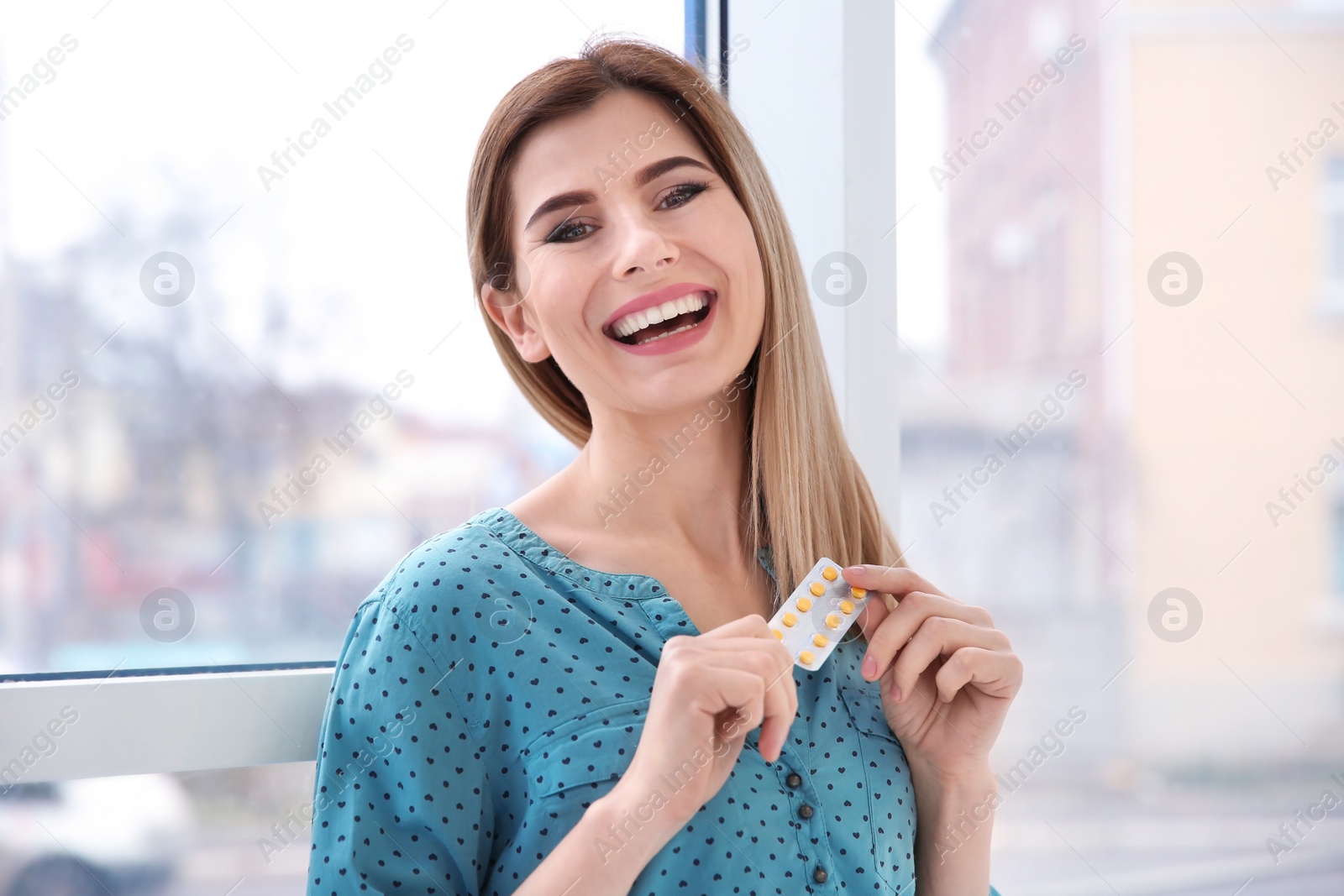 Photo of Young woman holding blister with vitamins indoors