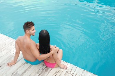 Photo of Woman in bikini with boyfriend near outdoor pool. Happy young couple