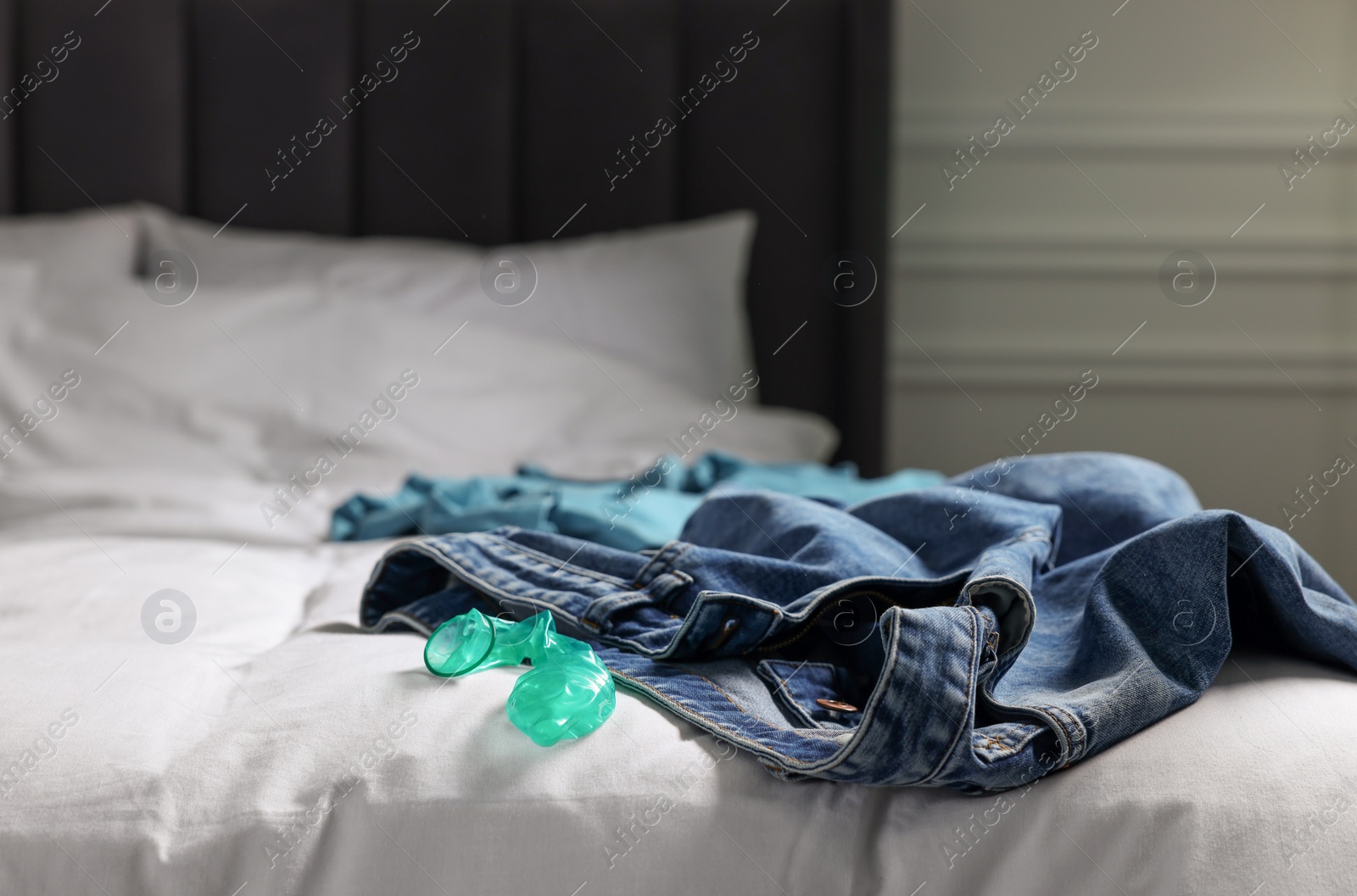 Photo of Unrolled condom and jeans on bed in bedroom. Safe sex