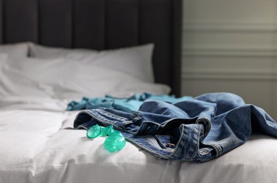 Photo of Unrolled condom and jeans on bed in bedroom. Safe sex