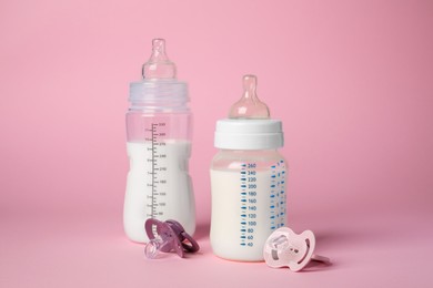 Photo of Feeding bottles with milk and baby pacifiers on pink background