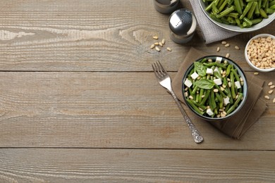 Photo of Delicious salad with green beans, pine nuts and cheese served on wooden table, flat lay. Space for text