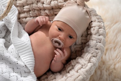 Photo of Adorable newborn baby with pacifier in wicker basket, above view