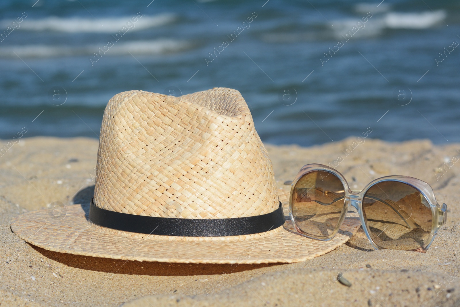 Photo of Stylish straw hat and sunglasses on sandy beach