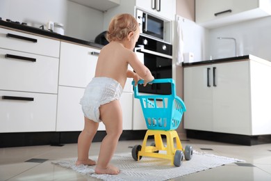 Cute baby with toy walker in kitchen. Learning to walk