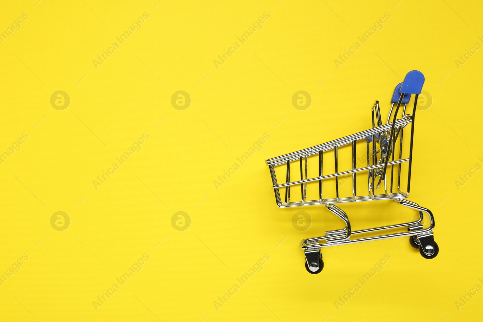 Photo of Small metal shopping cart on yellow background, top view. Space for text