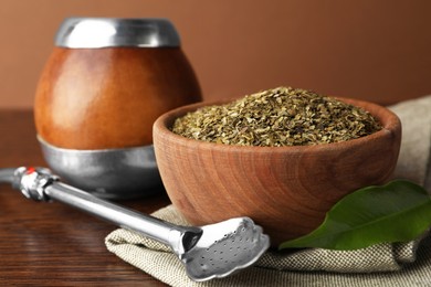 Photo of Bowl with mate tea and bombilla on wooden table, closeup