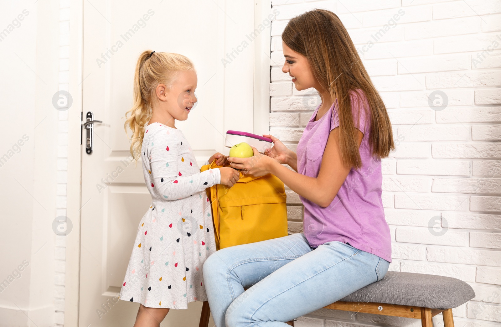 Photo of Young mother and little child putting lunch into school bag at home