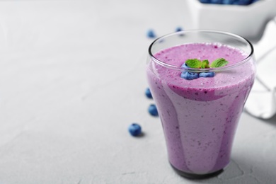 Photo of Glass of tasty blueberry smoothie on light grey table. Space for text