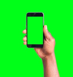 Image of African American man holding smartphone with green screen on color background, closeup. Mockup for design