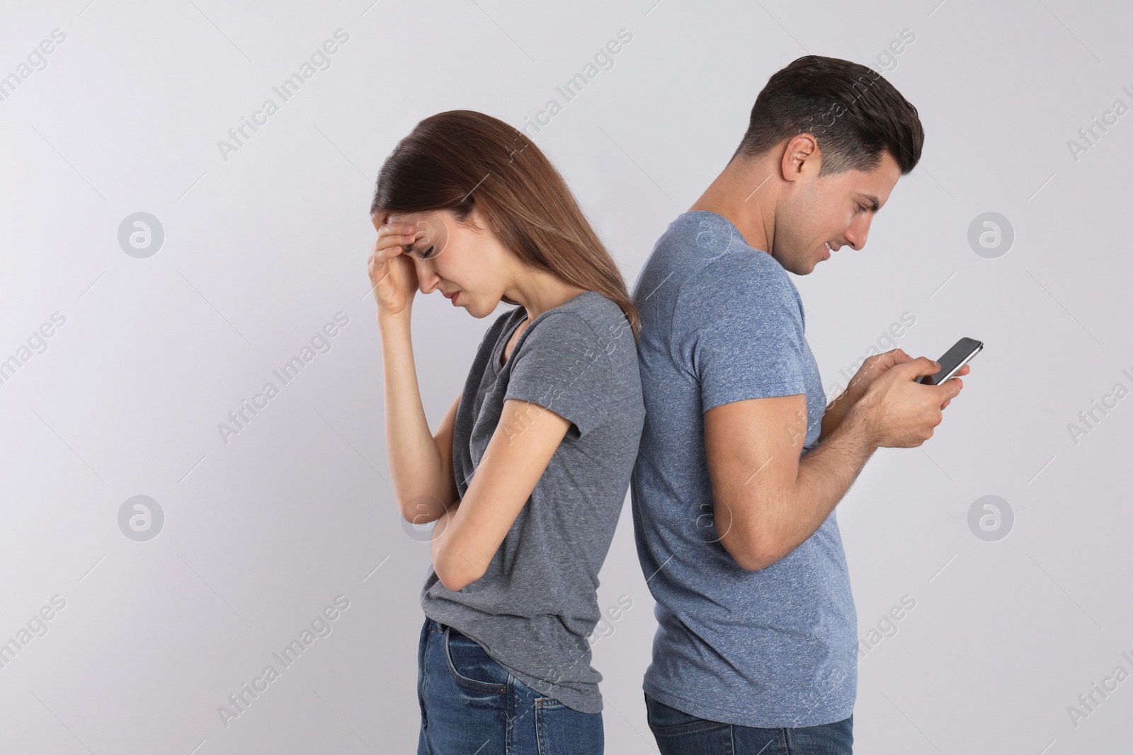 Photo of Man with smartphone ignoring his girlfriend on light background. Relationship problems