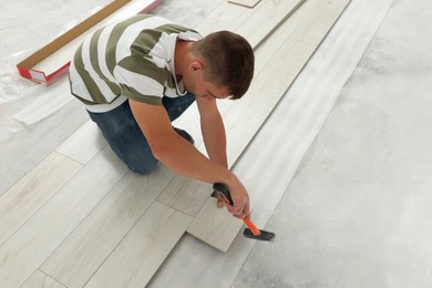 Photo of Professional worker using hammer during installation of new laminate flooring indoors