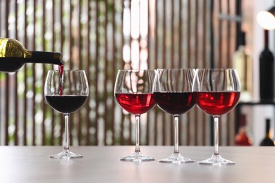 Photo of Pouring red wine from bottle into glass on table indoors