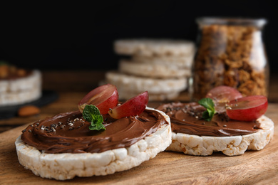 Photo of Puffed rice cakes with chocolate spread and grape on wooden board, closeup