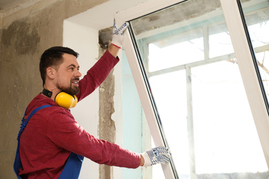 Photo of Worker in uniform installing plastic window indoors