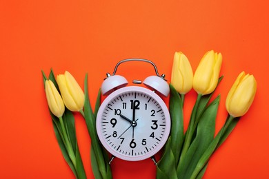 Photo of Pink alarm clock and beautiful tulips on orange background, flat lay. Spring time