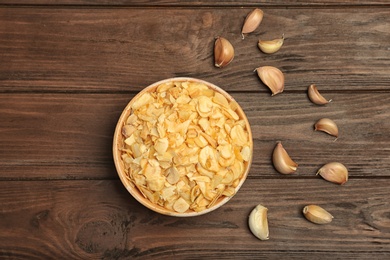 Photo of Cloves and bowl with dried garlic flakes on wooden background, top view