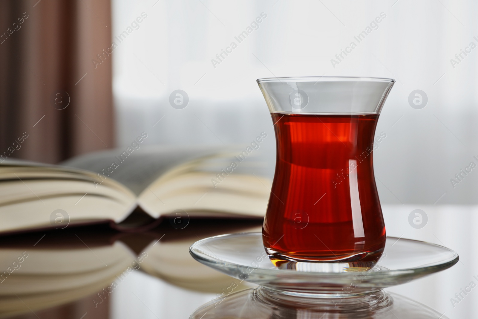 Photo of Glass with tasty Turkish tea and book on brown table indoors, closeup. Space for text