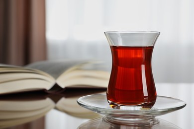 Glass with tasty Turkish tea and book on brown table indoors, closeup. Space for text