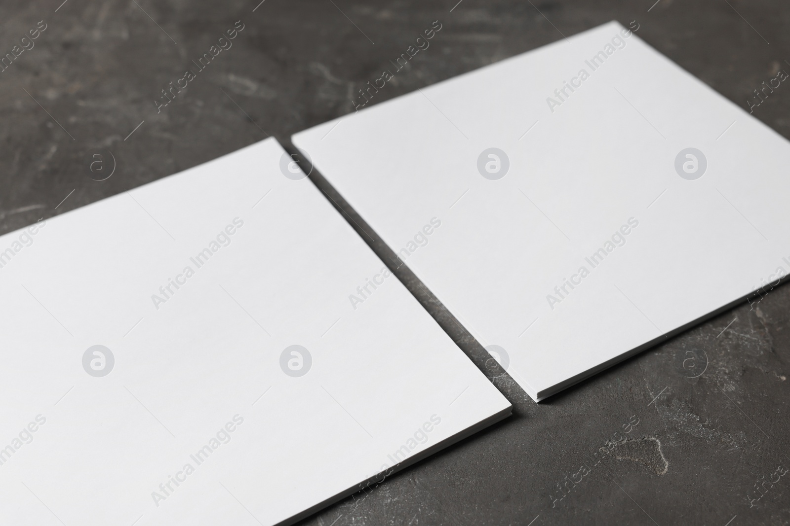 Photo of Blank paper sheets on grey textured table, closeup. Mockup for design