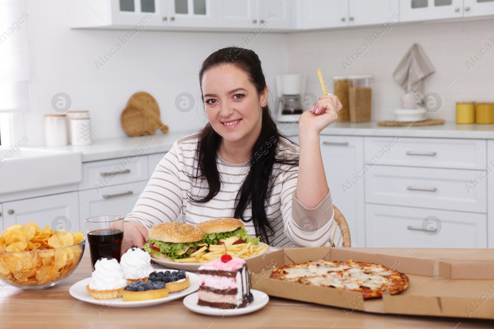 Photo of Happy overweight woman with unhealthy food in kitchen