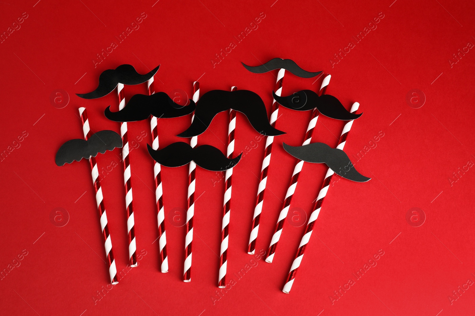 Photo of Fake paper mustaches with party props on red background, flat lay