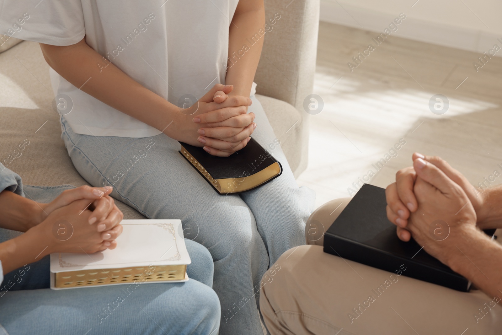 Photo of Group of religious people with Bibles praying together indoors, closeup