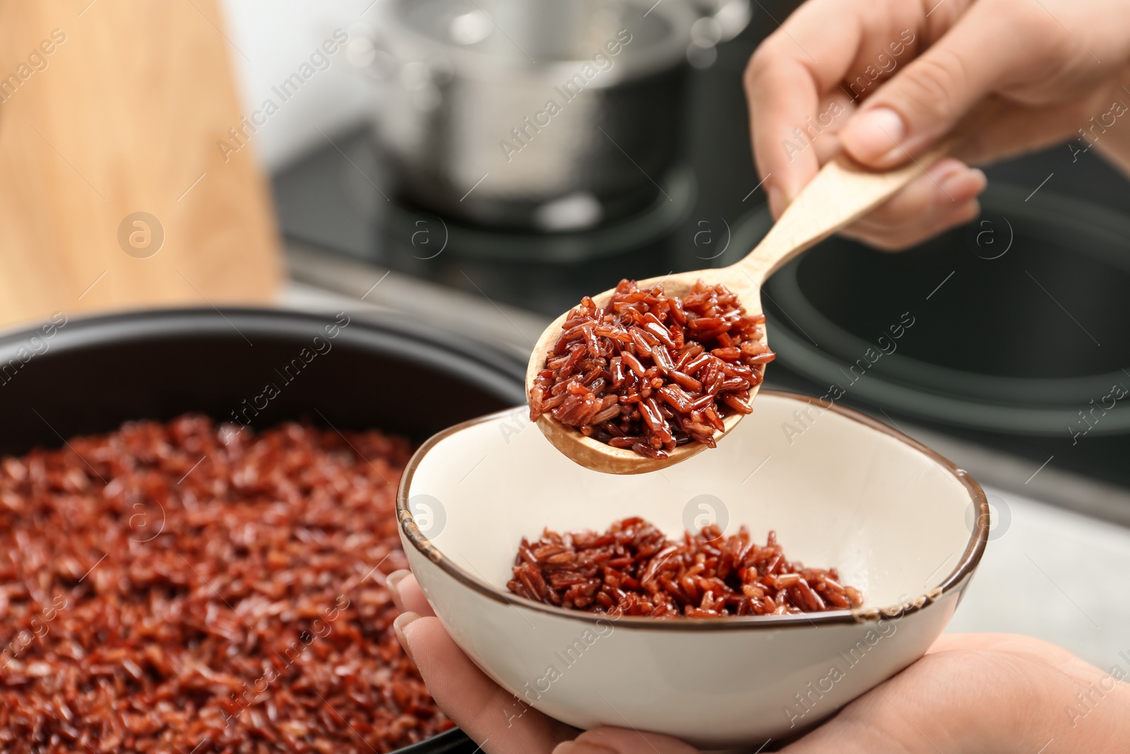 Photo of Woman putting brown rice into bowl from multi cooker in kitchen, closeup