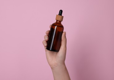 Woman holding bottle of cosmetic product on pink background, closeup