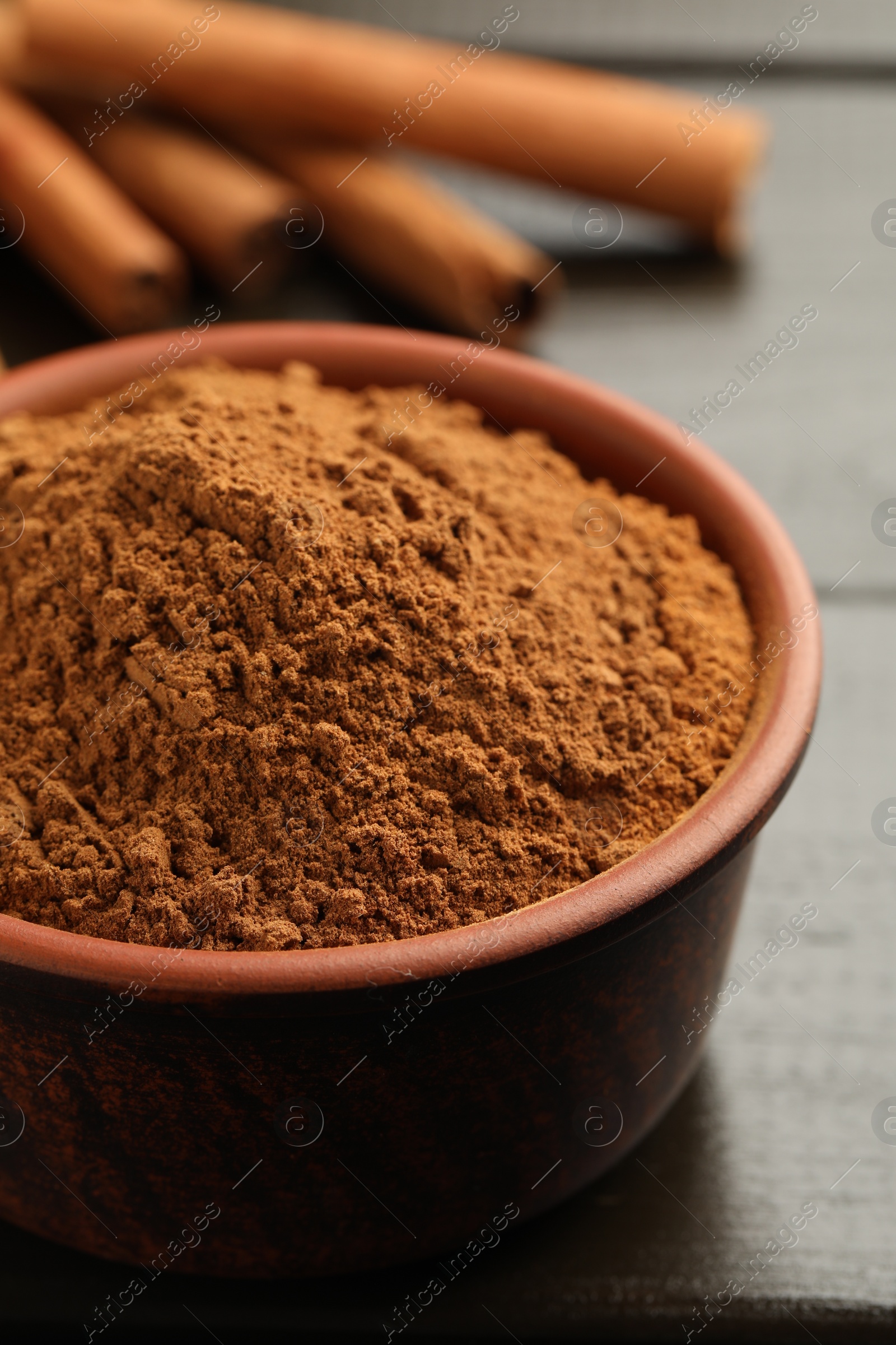 Photo of Bowl of cinnamon powder and sticks on wooden table, closeup
