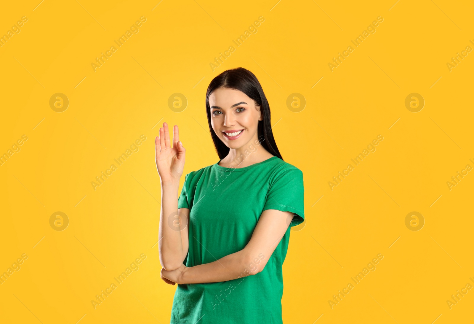 Photo of Attractive young woman showing hello gesture on yellow background