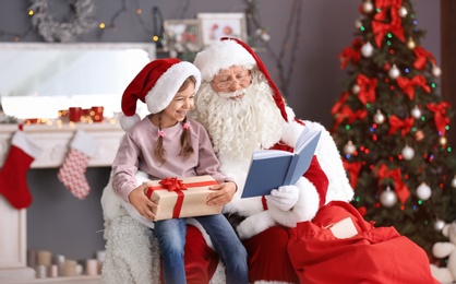 Photo of Authentic Santa Claus reading book to little girl indoors