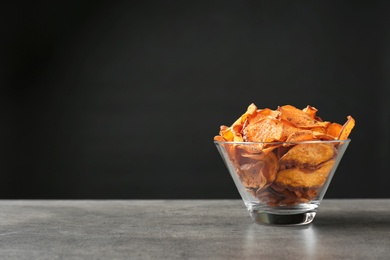 Photo of Bowl with sweet potato chips on table against black background. Space for text